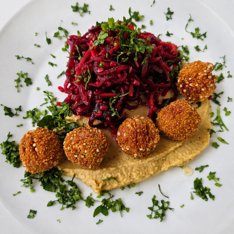 Veganes Gericht mit würzigem Rote-Bete-Salat, cremigem Hummus und knusprigen Falafel, garniert mit frischen Kräutern.