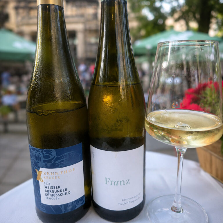 Zwei gekühlte Weißweine mit eingeschenktem Weinglas, sommerlich im Biergarten serviert.